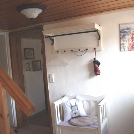 Ein hell eingerichteter Flur mit einer weißen Garderobe, einer Holztreppe, einer kleinen Sitzbank mit Hasenkissen und einer gemütlichen Holzdecke im Ferienhaus QuarTIER in Böchingen.