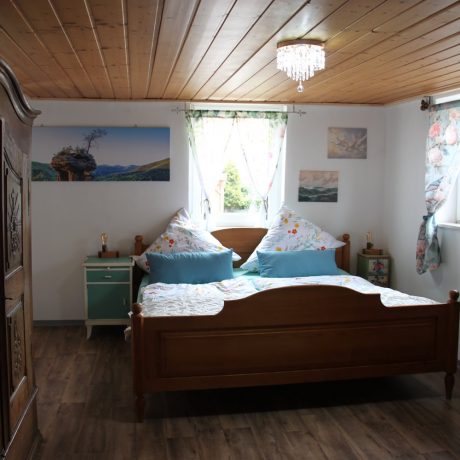 Ein gemütliches Schlafzimmer mit einem hölzernen Doppelbett, bezogenen Betten, Nachttischen, einem großen rustikalen Kleiderschrank und einer Holzdecke im Ferienhaus QuarTIER in Böchingen.