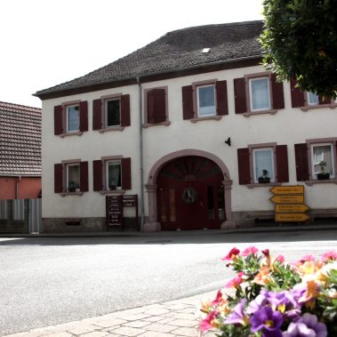 Ein großes, historisches Gebäude mit braunen Fensterläden und einem großen Rundbogentor an einer Kreuzung in Böchingen.